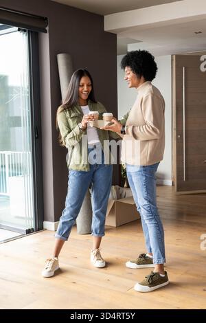 Remise de tasses à café, couple diversifié déballage boîte en carton dans le salon, avec tapis de yoga Banque D'Images