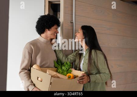 Boîte de transport de produits d'épicerie, couple diversifié partageant un moment affectueux à l'entrée de la maison Banque D'Images