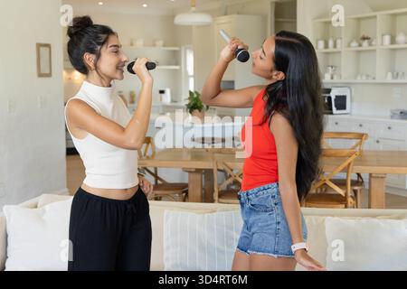 Chanter diverses amies féminines debout dans un espace de vie ouvert, avec des microphones sans fil Banque D'Images