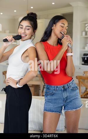 Chanter diverses amies faisant du karaoké dans un salon et une cuisine ouverts, avec des micros Banque D'Images