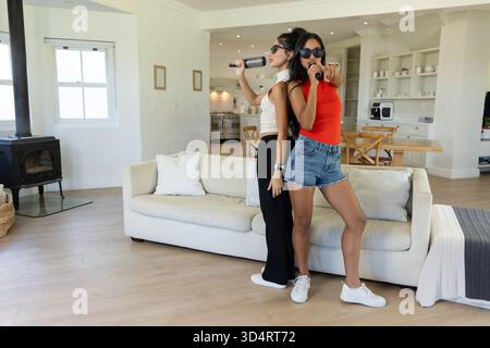 Chanter diverses amies debout dos à dos dans le salon, avec brosse à cheveux et microphone Banque D'Images