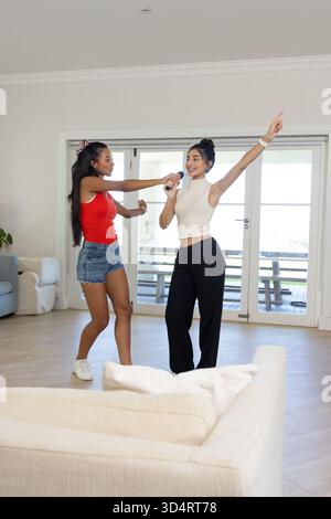 Chant karaoké diverses amies féminines dansant dans le salon, avec microphone sans fil et plante Banque D'Images