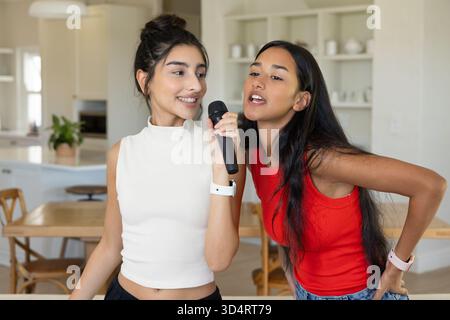 Chanter diverses amies féminines debout dans la cuisine moderne de la maison et la salle à manger, avec microphone Banque D'Images