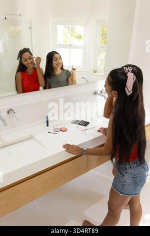 Application du mascara, eyeliner divers amis féminins debout à l'évier de salle de bain, avec palette de fards à paupières Banque D'Images