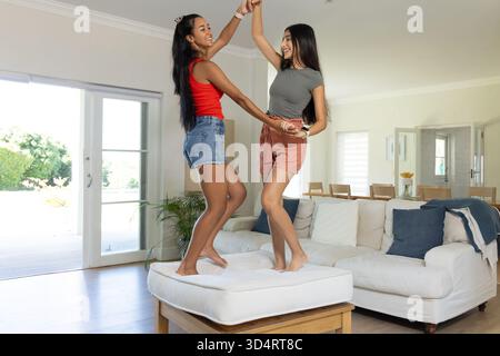 Danser diverses amies féminines sur pouf blanc dans le salon moderne, avec des oreillers de jet Banque D'Images