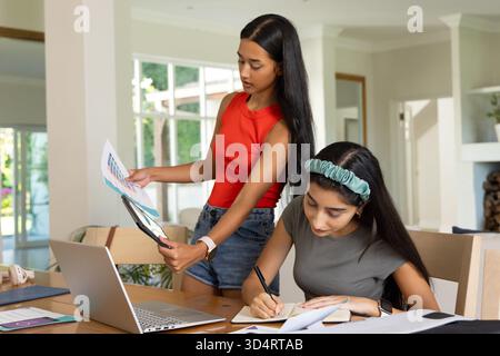 Collaboration de diverses amies féminines arrangeant des échantillons de couleurs et écrivant dans l'espace de travail, avec un ordinateur portable Banque D'Images
