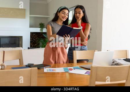 Collaboration diverses amies féminines examinant le cahier dans le salon, avec ordinateur portable et échantillons Banque D'Images