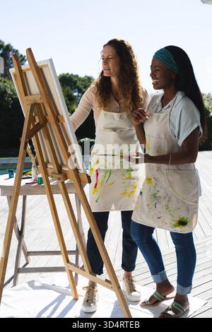 Peinture diverses amies féminines collaborant sur toile au chevalet sur le pont avec palette et pinceaux Banque D'Images