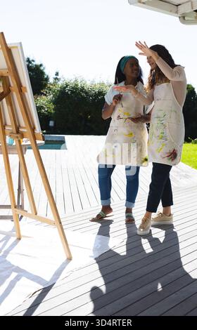 Peinture diverses amies féminines collaborant sur la toile de chevalet à la terrasse arrière, avec palette de peinture Banque D'Images