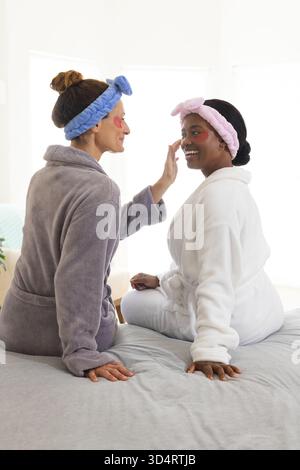 Choyer diverses amies féminines en appliquant des patchs rouges sous les yeux sur le lit, avec des bandeaux en peluche Banque D'Images