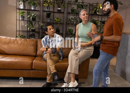 Bavarder divers collègues assis sur le canapé en cuir dans le salon de bureau, avec des tasses à café et des plantes Banque D'Images