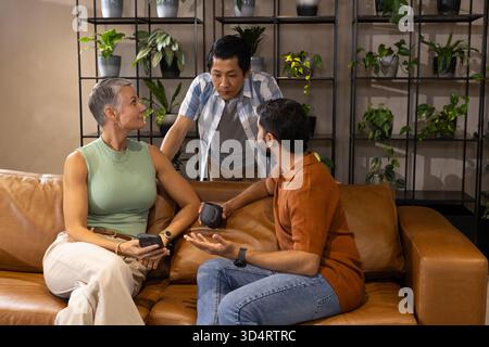 Discuter du projet divers collègues assis sur le canapé dans le salon, avec tasse à café smartphone Banque D'Images