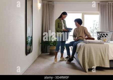 Vêtements pliants de couple diversifiés dans une chambre moderne, avec panier à linge et plante, espace copie Banque D'Images
