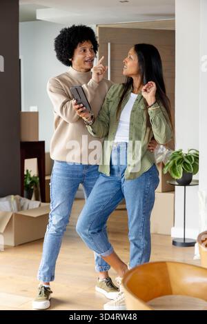 Parler couple diversifié déballer des boîtes en carton dans un salon moderne ouvert, avec smartphone Banque D'Images