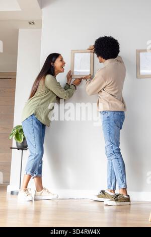 Accrocher divers couples ajustant le cadre d'image en bois sur le mur de couloir, avec table d'appoint et plante Banque D'Images