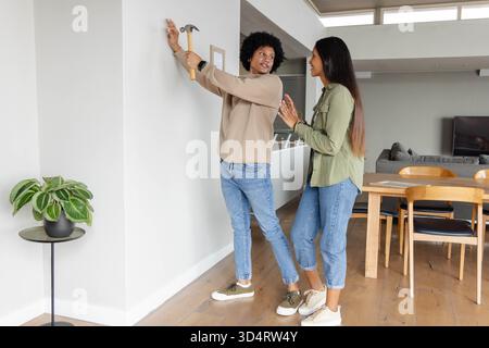 Cadre d'image suspendu de couple diversifié sur le mur dans le salon décloisonné, avec marteau et plante Banque D'Images