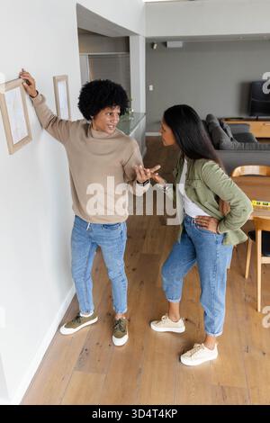 Accrocher divers couples ajustant le cadre photo en bois sur le mur dans le salon, avec niveau à bulle Banque D'Images
