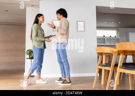 Argumentant couple diversifié debout dans le salon moderne, avec plante en pot et table Banque D'Images