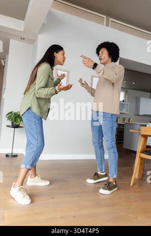Argumentant couple diversifié debout dans la maison ouverte, avec smartwatch et plante en pot Banque D'Images