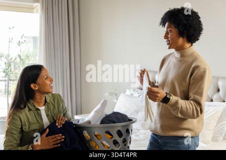 Divers couples triant et pliant le linge dans une chambre lumineuse, avec panier à linge en plastique et lit Banque D'Images