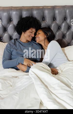 Blotti couple diversifié couché dans la chambre, avec couette blanche et tête de lit touffetée Banque D'Images