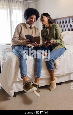 Examen couple diversifié assis sur le lit dans une chambre à coucher éclairée, avec passeport et smartphone Banque D'Images