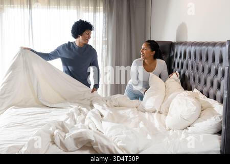 Housse de couette relevable, divers couples arrangeant les oreillers sur un grand lit dans la chambre avec tête de lit touffetée Banque D'Images