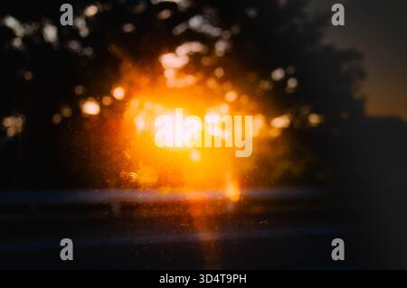 Coucher de soleil vu à travers une fenêtre de voiture avec une lumière brillante chaude et des silhouettes floues d'arbres. Banque D'Images