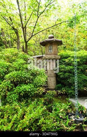 Lanterne en pierre entourée de verdure luxuriante le long d'un chemin de jardin à Himeji. Banque D'Images