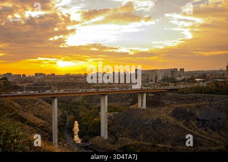 Un pont enjambe une rivière avec une ville en arrière-plan. Le ciel est orange et le soleil se couche Banque D'Images