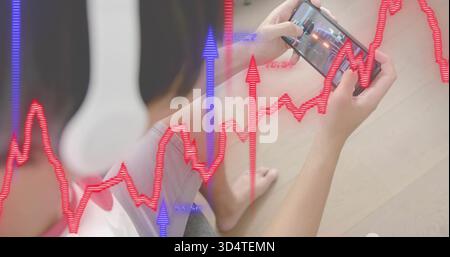Assis homme asiatique dans le short gris blanc haut sur le sol tenant le téléphone avec casque, superpositions financières Banque D'Images