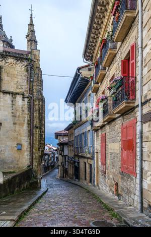 Rue pavée étroite, bâtiments colorés, balcons de fleurs, Tour historique de l'église, architecture médiévale, Hondarribia, pays Basque, Espagne Banque D'Images