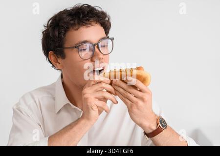 Jeune homme d'affaires mangeant un hot dog savoureux au bureau, gros plan Banque D'Images