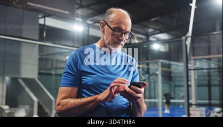 Padel, homme senior et SMS avec téléphone sur le terrain pour le point sur le match, les performances de piste ou les pauses de match. Retraite fitness, personne âgée et smartphone at Banque D'Images