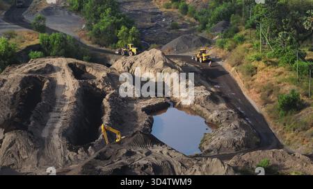 Exploitation de carrières avec des pelles hydrauliques, des bulldozers et des chargeuses sur pneus déplaçant le sable et les tas de sol, façonnant le terrain autour d'une fosse remplie d'eau dans un site minier actif à ciel ouvert. Concept industriel. Panorama aérien Banque D'Images