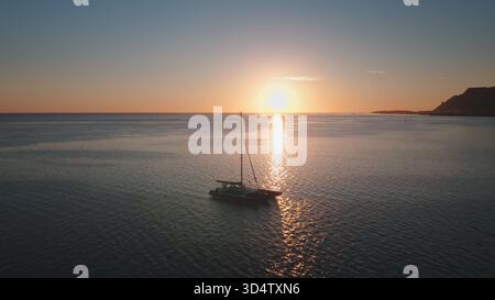 Superbe vue aérienne de deux catamarans à voilier ancrés sur des eaux tranquilles près d'une île tropicale en Polynésie française. Ciel de coucher de soleil coloré en arrière-plan. Voyage d'été exotique dans la nature sauvage éloignée Banque D'Images