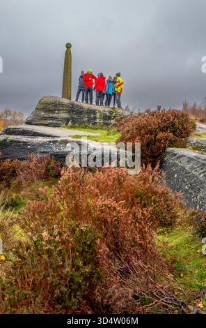 Un groupe de marcheurs debout sur le côté du Nelson's Monument sur un éperon rocheux dans le Derbyshire Peak District par un froid jour d'automne. Banque D'Images