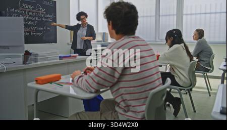 Une enseignante confiante explique les tâches d'encodage aux élèves. Les adolescents écoutent attentivement, prennent des notes et discutent des idées. Éducation STEM moderne, travail d'équipe, environnement d'apprentissage innovant. Dolly Shot. Banque D'Images