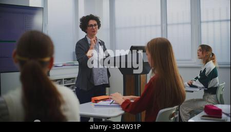 Éducateur féminin dans la classe de programmation informatique présente le code logiciel sur Smartboard, engageant les étudiants dans la discussion. Concept STEM Education, apprentissage interactif et innovation dans les méthodes d'enseignement. Banque D'Images
