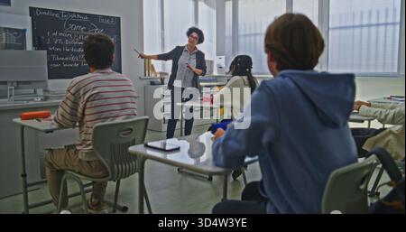 Une enseignante se tient près de Blackboard expliquant l'affectation de codage à un groupe d'étudiants dans la classe lumineuse. Concept de l'éducation moderne, apprentissage interactif, travail d'équipe créatif dans l'environnement scolaire. Banque D'Images