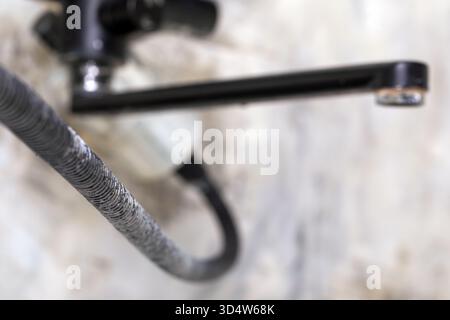 Vue détaillée d'un tuyau métallique enroulé sur un robinet industriel moderne, avec un fond de marbre flou. Convient pour la plomberie, la rénovation ou l'intérieur d Banque D'Images