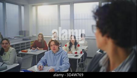Gros plan femme adulte portant des lunettes écrit activement avec marqueur sur le tableau interactif invisible. Les élèves écoutent attentivement. Concept de méthodes d'enseignement modernes, innovations en technologie éducative. Banque D'Images