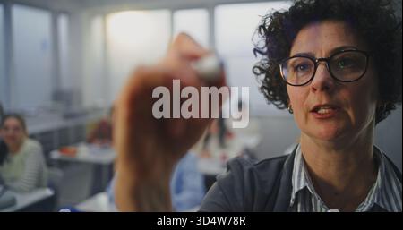 Gros plan femme adulte portant des lunettes écrit activement avec marqueur sur le tableau interactif invisible. Les élèves écoutent attentivement. Concept de méthodes d'enseignement modernes, innovations en technologie éducative. Banque D'Images