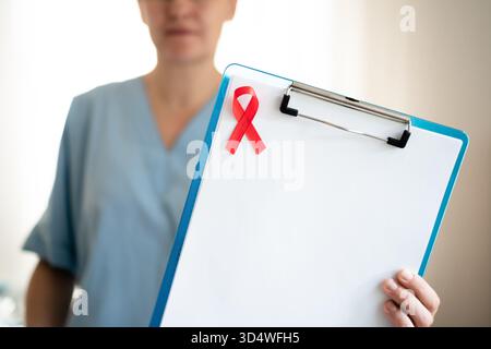 Professionnel de la santé amical avec ruban rouge de sensibilisation au SIDA contenant des formulaires médicaux, montrant des soins compatissants pour les patients VIH et la communauté. Banque D'Images