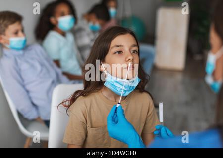 La fille subit un test de coronavirus avec un groupe d'enfants en milieu clinique Banque D'Images