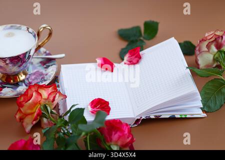 Matinée romantique avec des roses, un cahier et une tasse de cappuccino. Banque D'Images