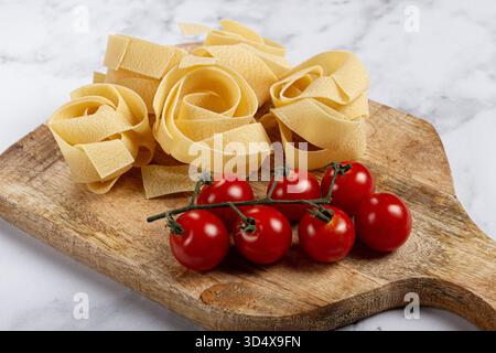 pâtes pappardelle crues, sur une planche à découper en bois, avec tomates cerises, vue de dessus, pas de gens, Banque D'Images