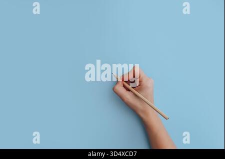 Main de femme tenant le crayon sur fond bleu, espace de copie pour le texte ou la conception. Banque D'Images
