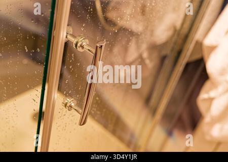 Une porte de douche transparente contient de nombreuses gouttelettes minuscules qui s'accrochent à la vitre propre après le lavage, des stries douces attrapent la lumière et la salle de bain se sent qui Banque D'Images