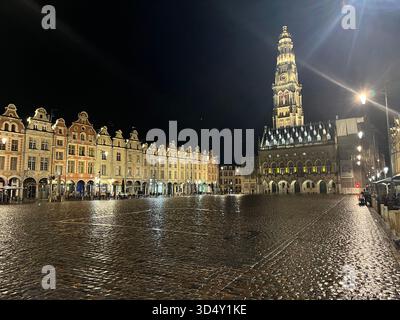 Grand place à Arras, France, la nuit avec l'hôtel de ville illuminé et le beffroi reflétés sur les pavés humides Banque D'Images